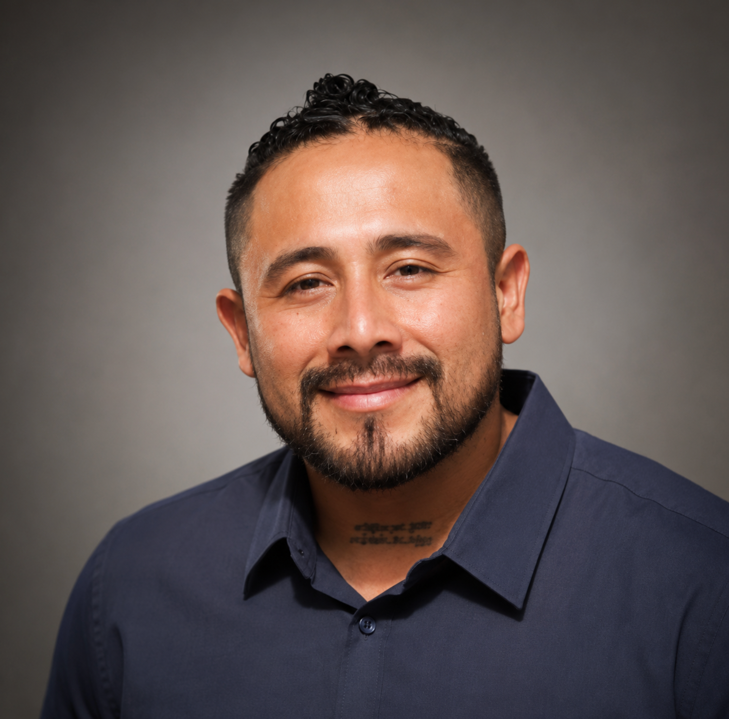 Smiling man in a dark blue shirt against a gray studio backdrop
