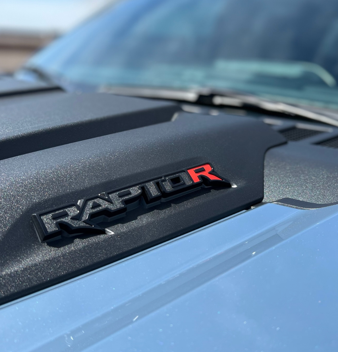 Close-up of a Ford Raptor hood badge in black and red on a blue truck.