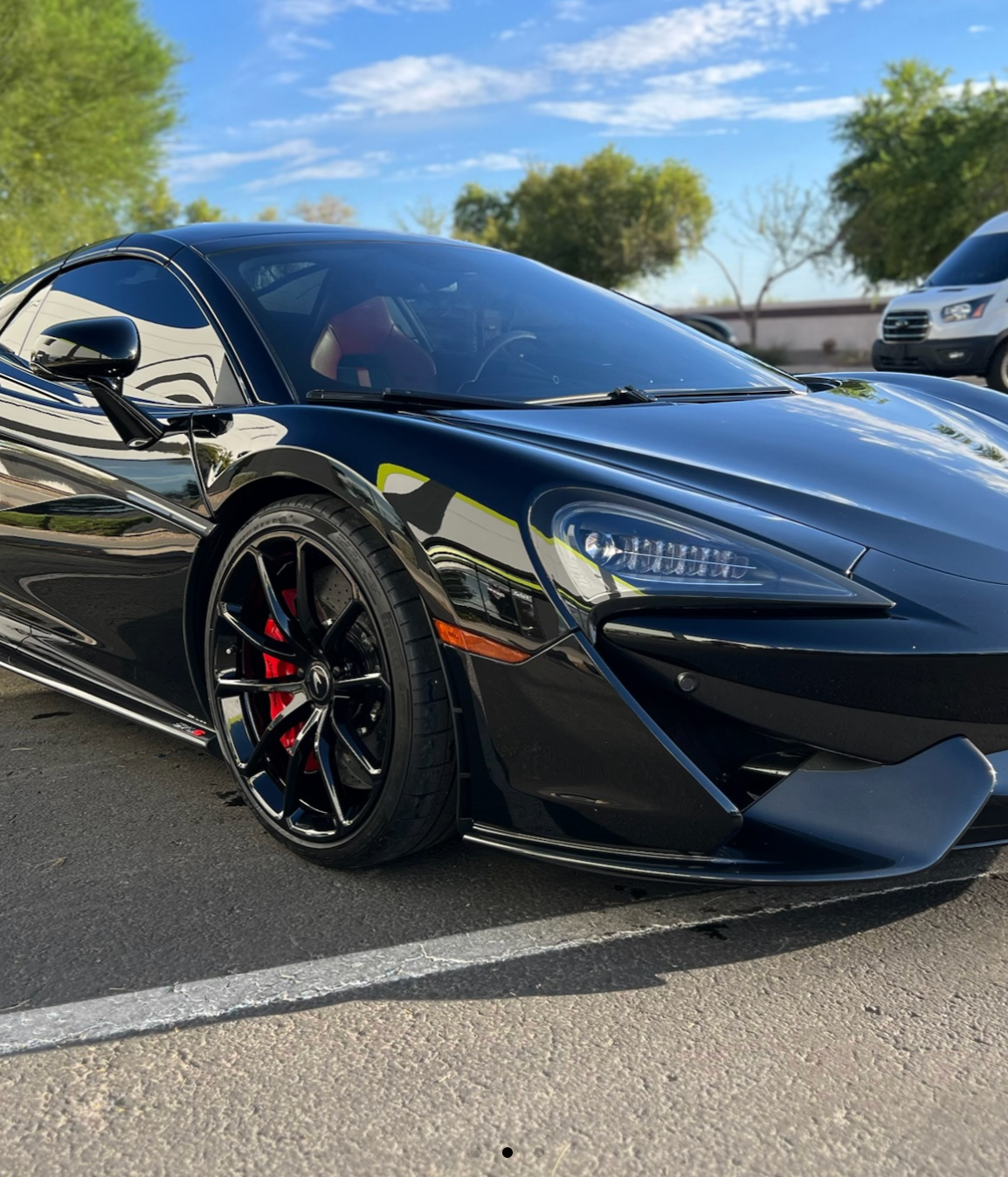 Black sports car with red brake calipers parked outdoors on a sunny day