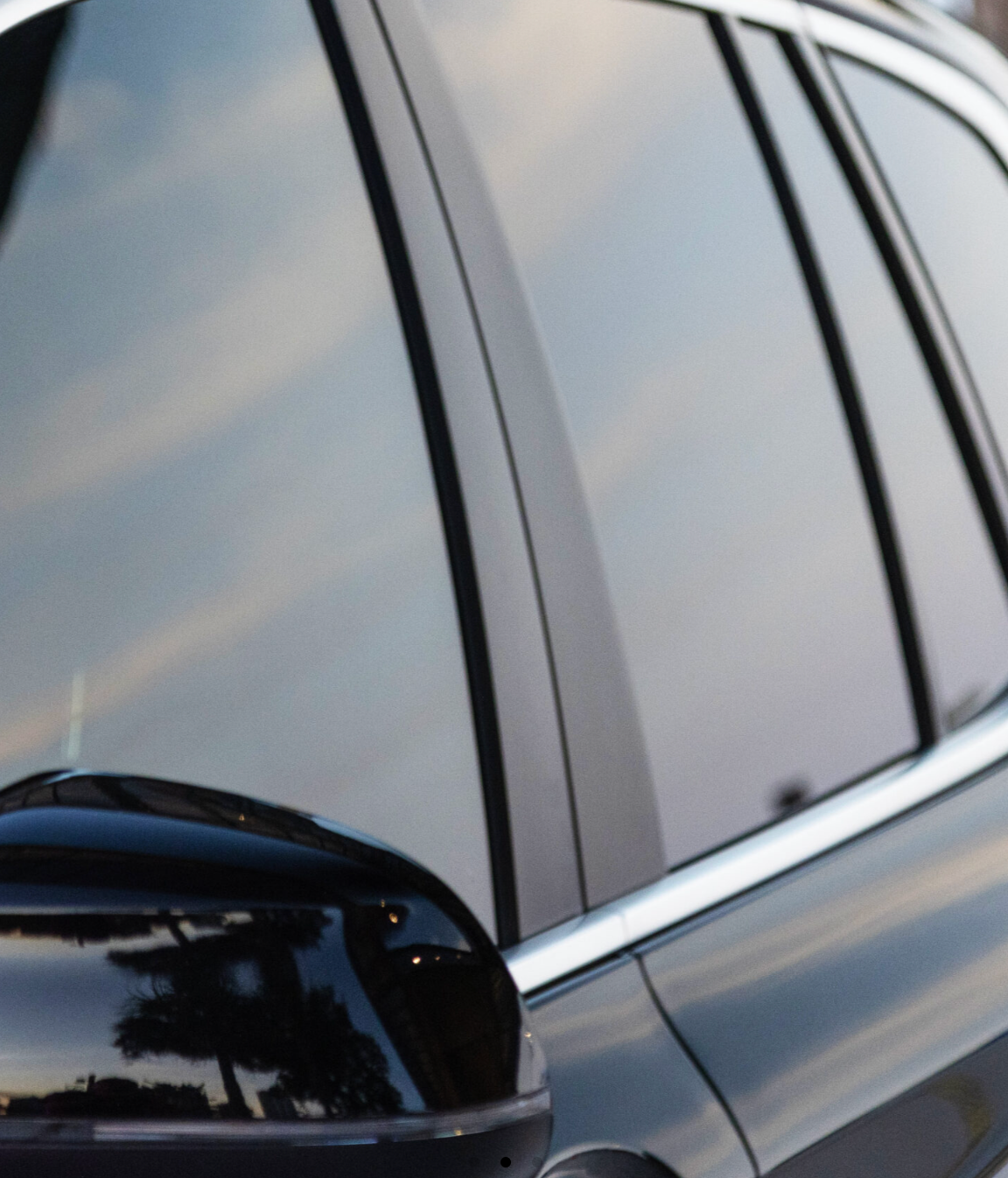 Close-up of a black car’s side mirror and tinted window reflecting the sky