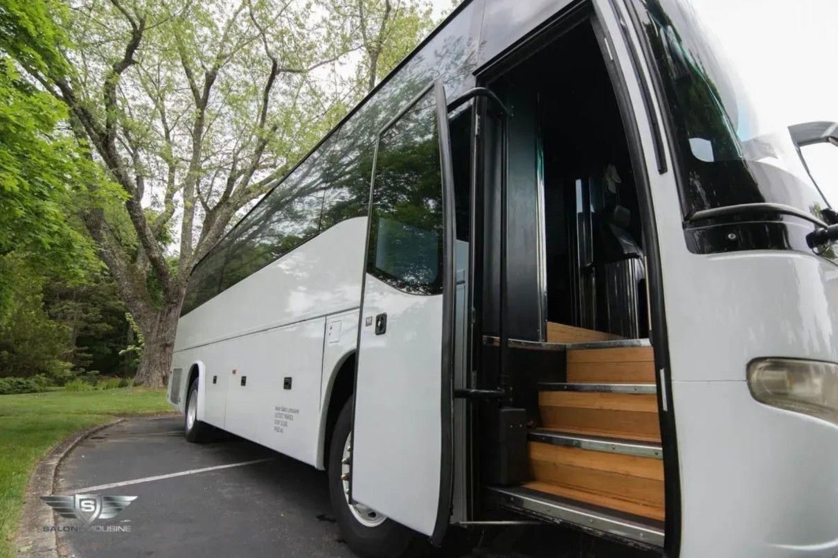 White passenger bus with open door, parked on pavement, steps leading up.