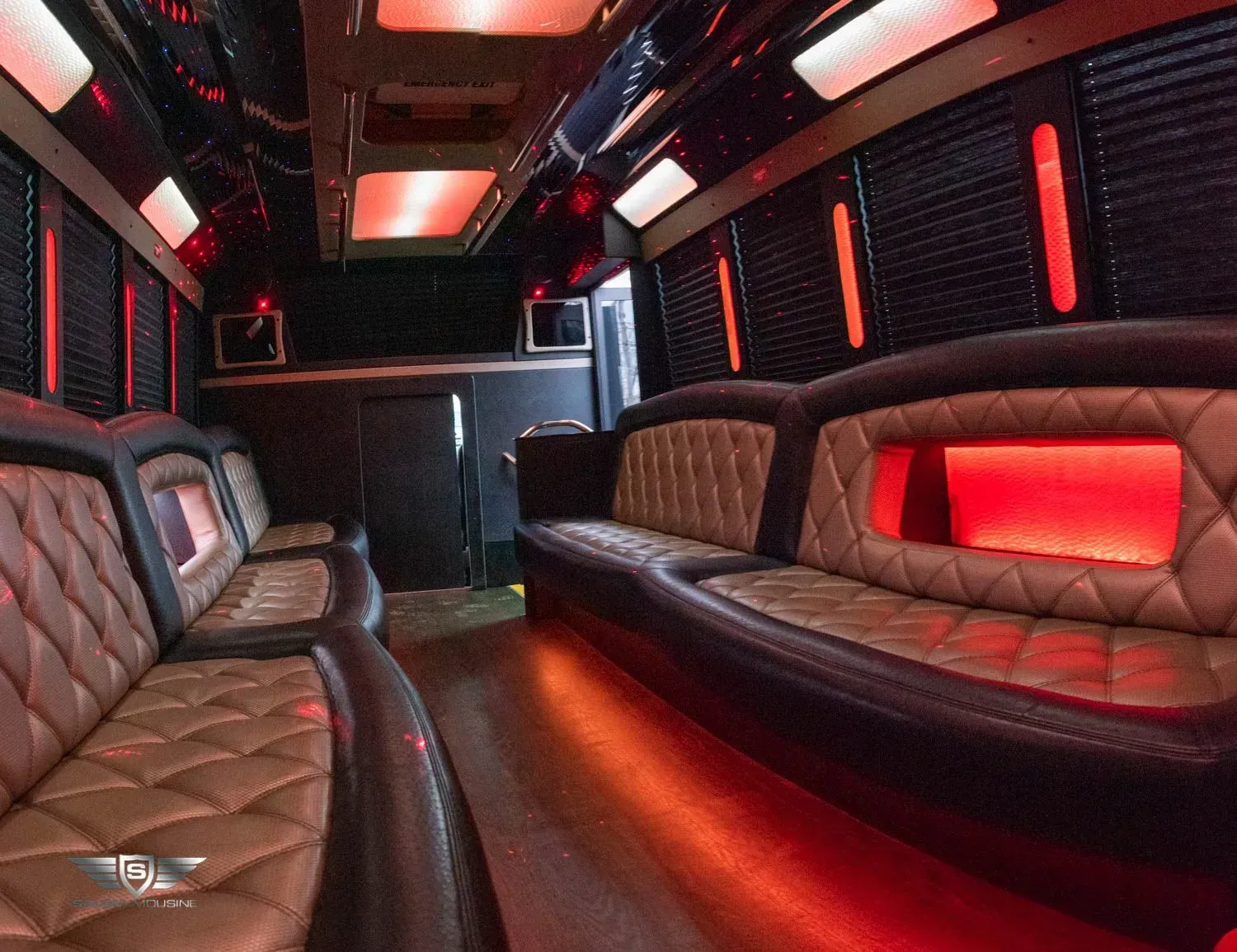 Interior of a party bus with brown leather seating, red lighting, and a bar area.