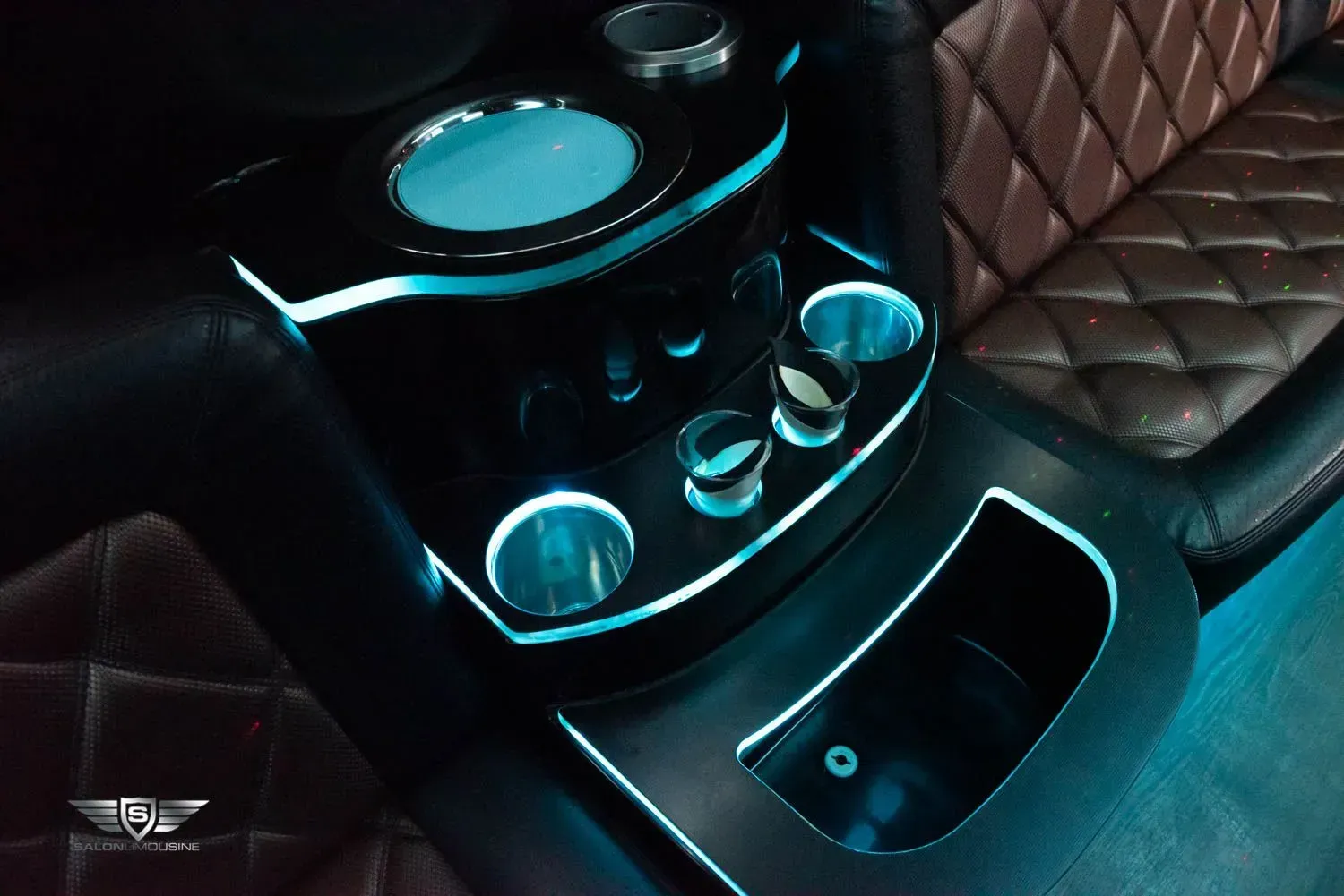 Inside of a limousine, a black bar area with teal glowing lights and cup holders.
