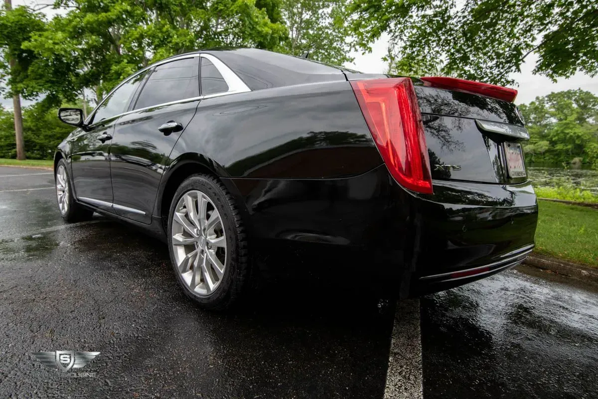 Black sedan parked on wet asphalt. Red taillights and silver rims are visible.