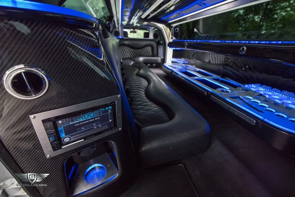 Interior of a luxury limousine, black leather seating, blue neon lights, carbon fiber accents, stereo system.