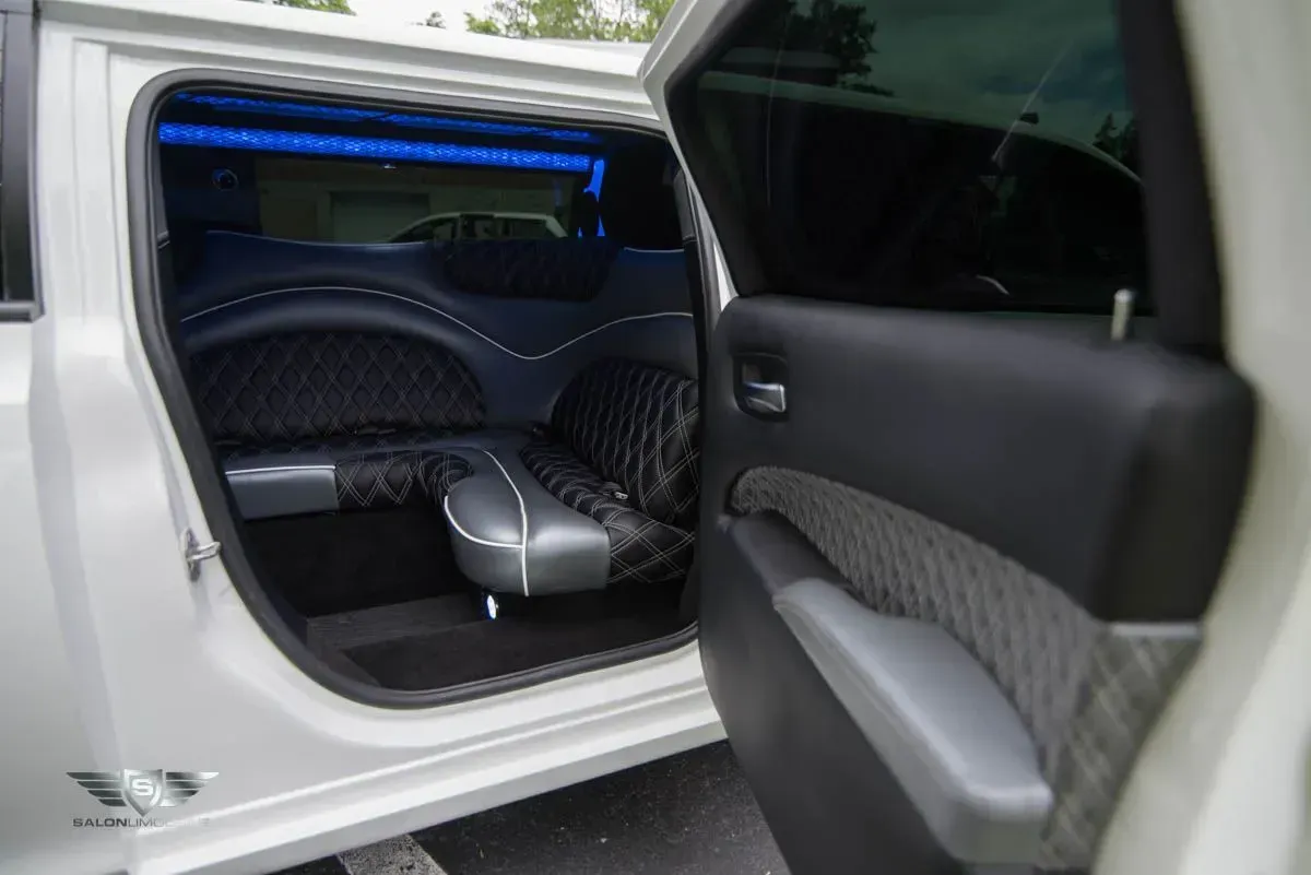 Interior of a white limousine with quilted black seats, blue lights, and an open door.