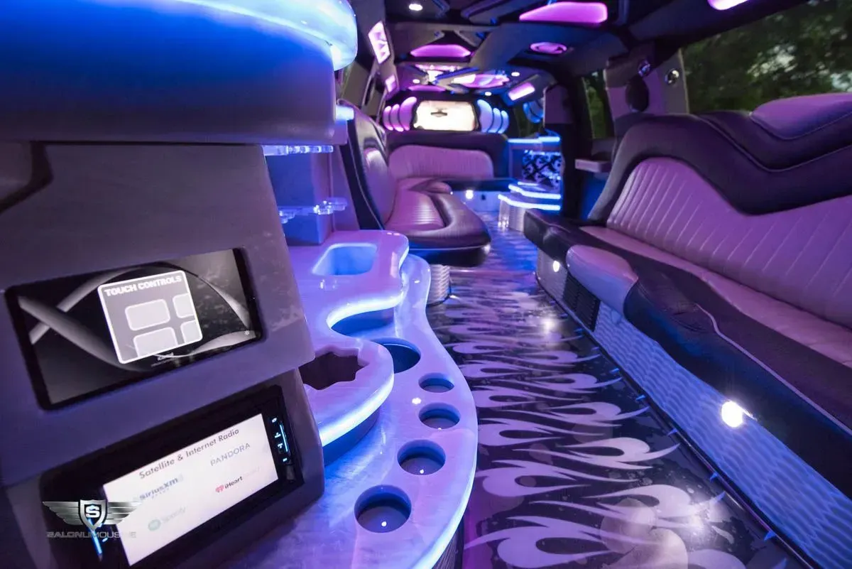 Interior of a limousine with neon blue and purple lighting, sleek design, built-in screens, and flame pattern on the floor.
