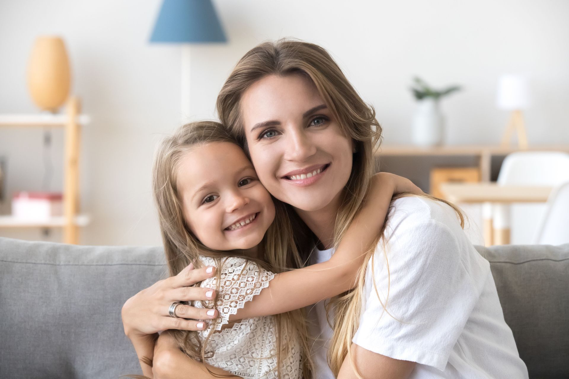 Woman and child smiling and hugging on a couch in a bright living room