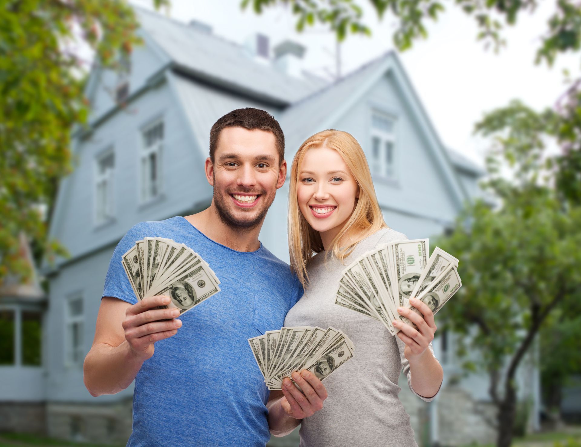 Smiling couple holding cash in front of a house for sale