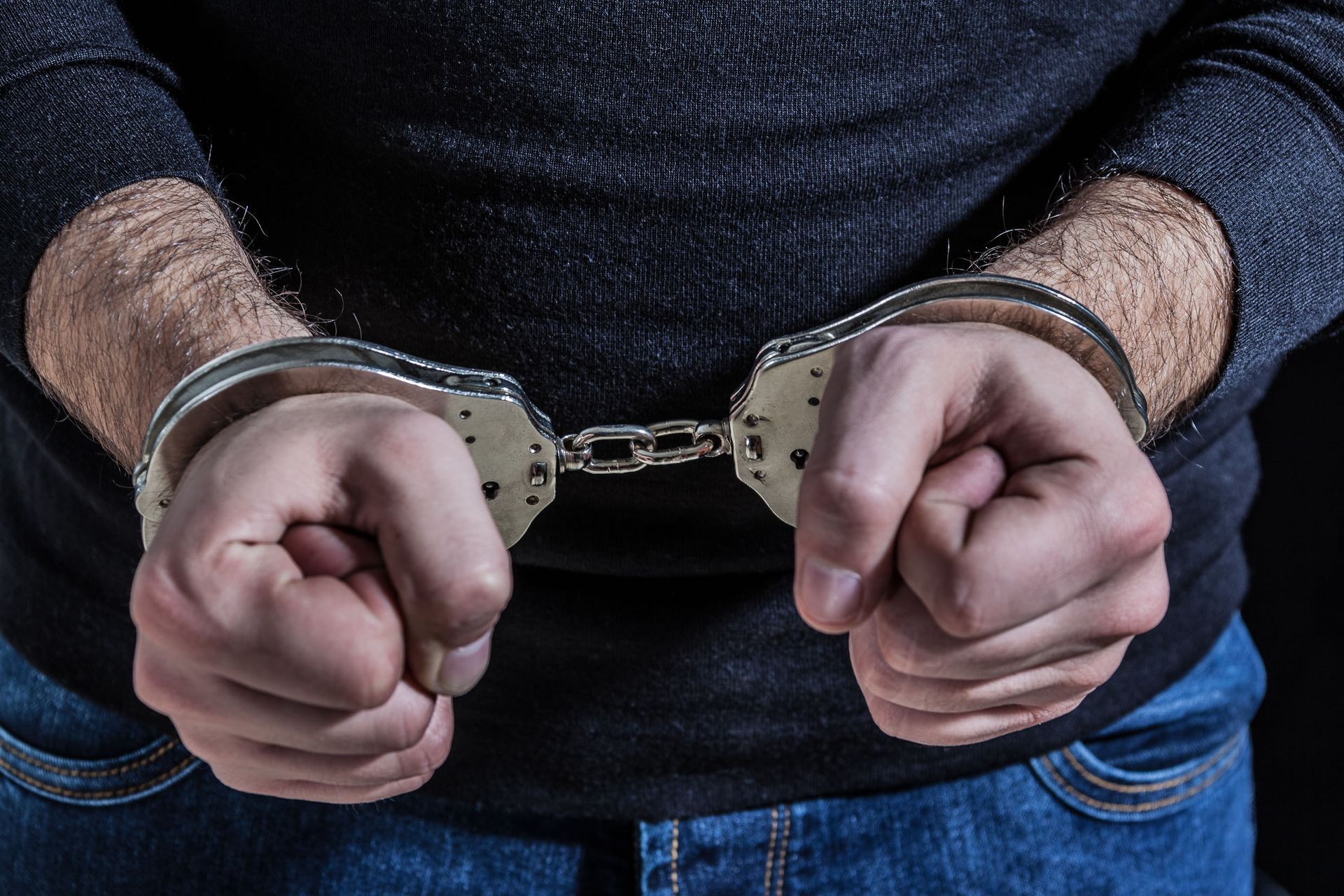 Handcuffed hands in front of a person wearing a dark shirt and jeans