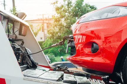 Red car being loaded onto a tow truck in a sunny roadside scene