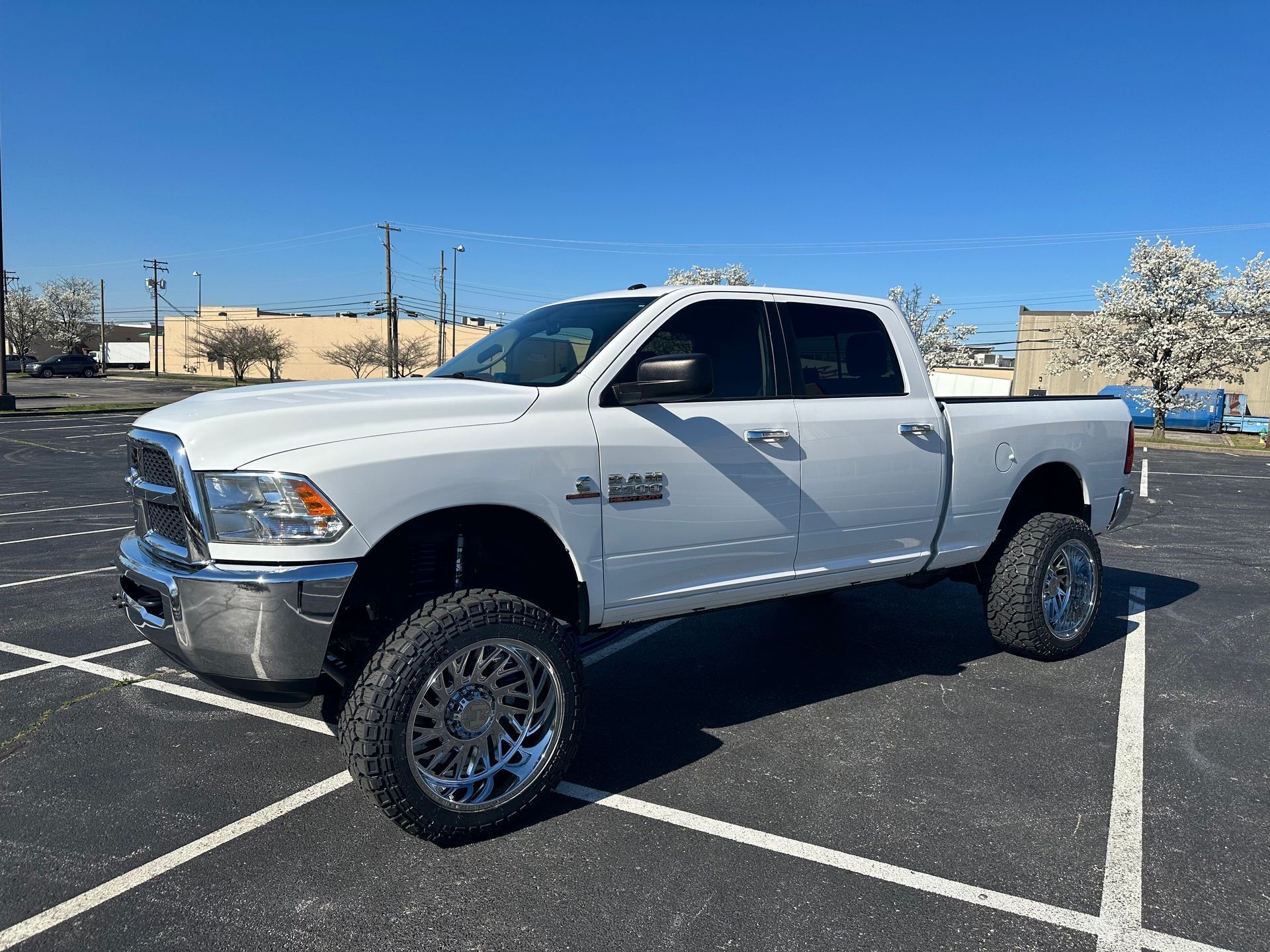 White lifted Dodge pickup truck parked in a sunlit lot with desert mountains in the background