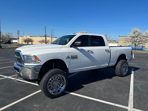 White lifted Dodge pickup truck parked in a sunlit lot with desert mountains in the background