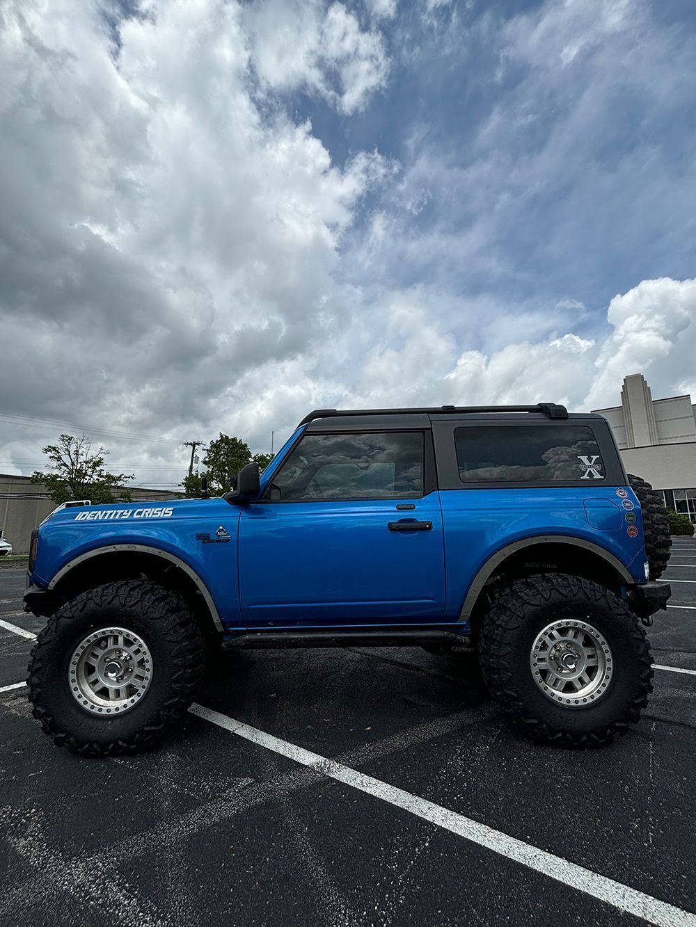 Blue off-road SUV with large tires parked in a wet parking lot under cloudy skies