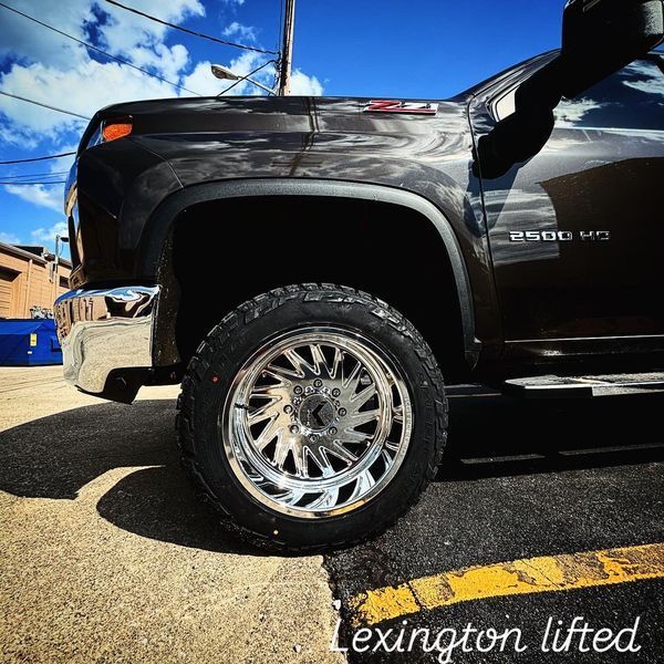 Black lifted Chevrolet pickup truck with chrome wheels parked outdoors under a blue sky