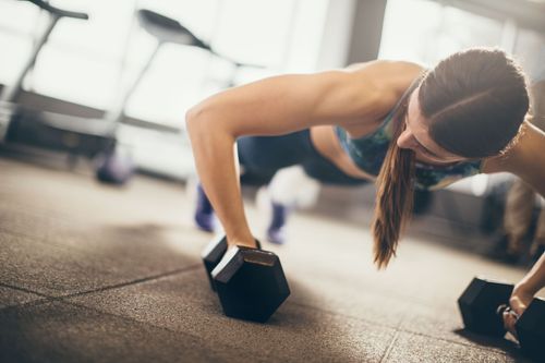 A woman is doing push ups with a dumbbell in a gym.