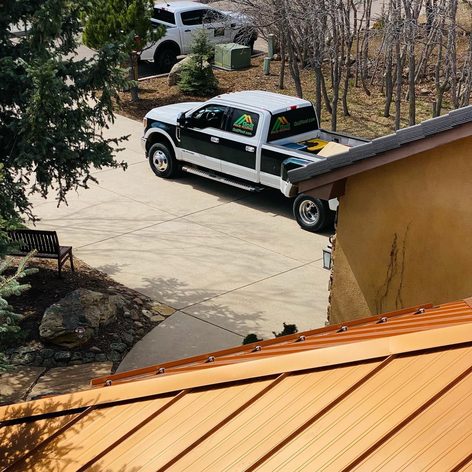 A white and green truck parked in a driveway near a house with a copper roof.