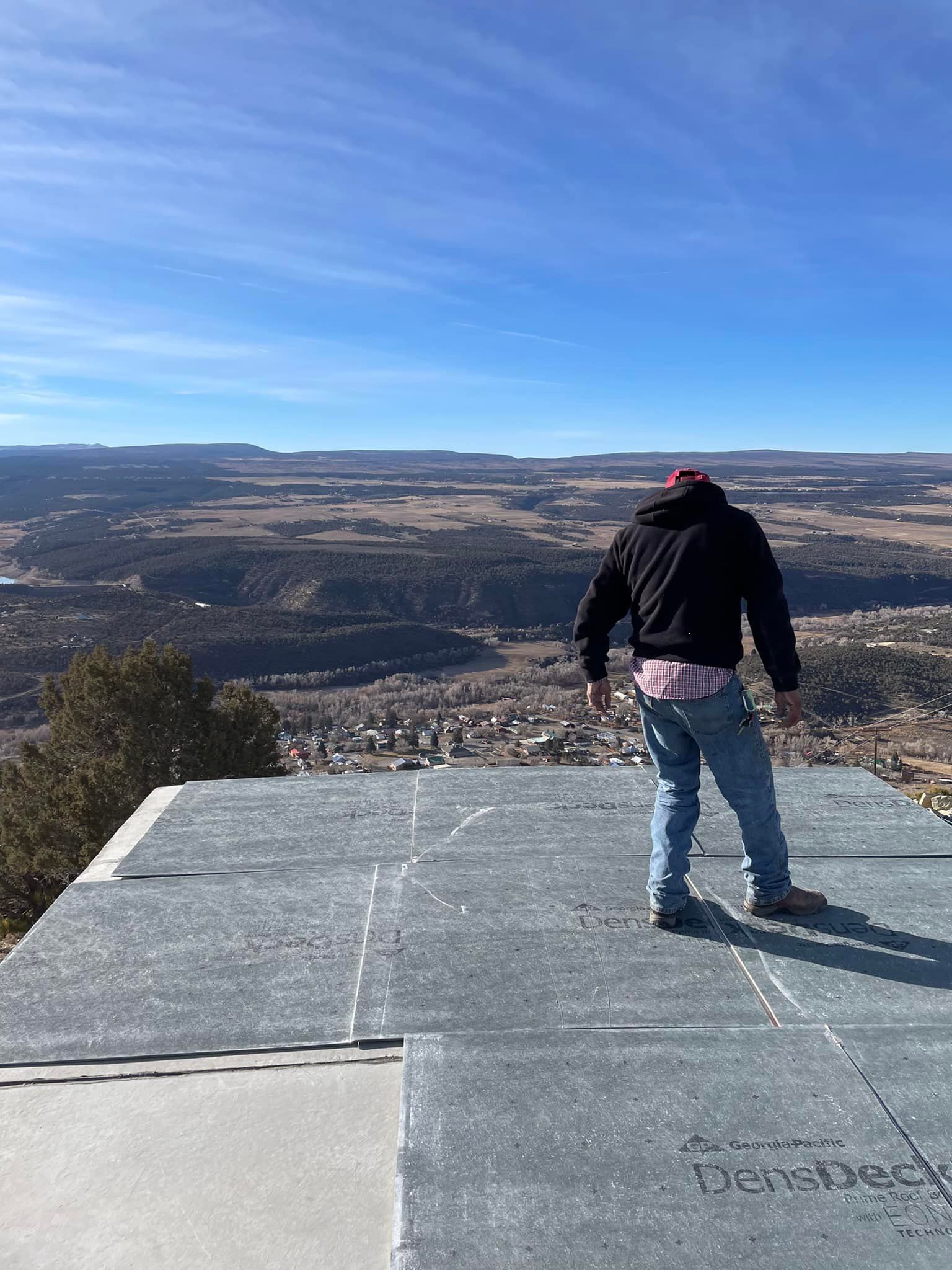 Person standing on rooftop overlooking a valley and town on a clear day.