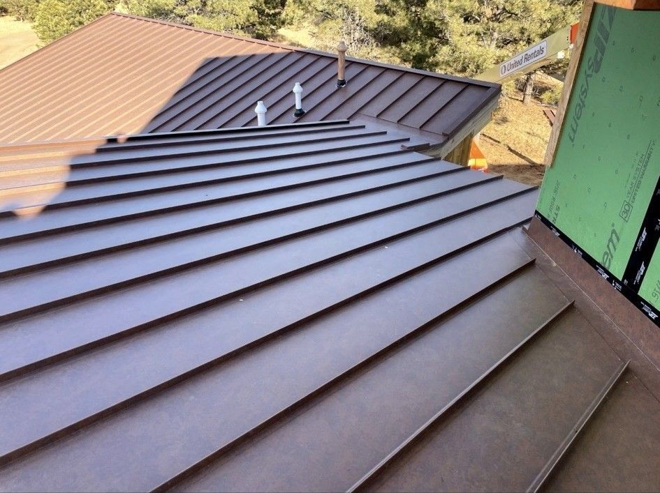 Brown metal roof panels on a building under construction with wood and green sheathing.