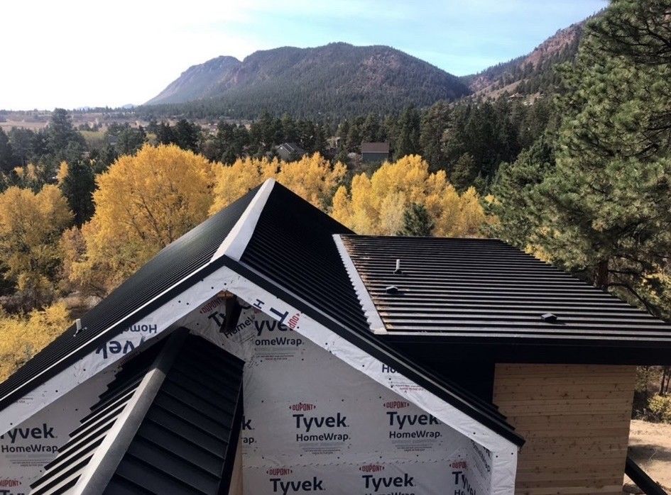 A black metal roof under construction in a mountain setting with fall foliage.