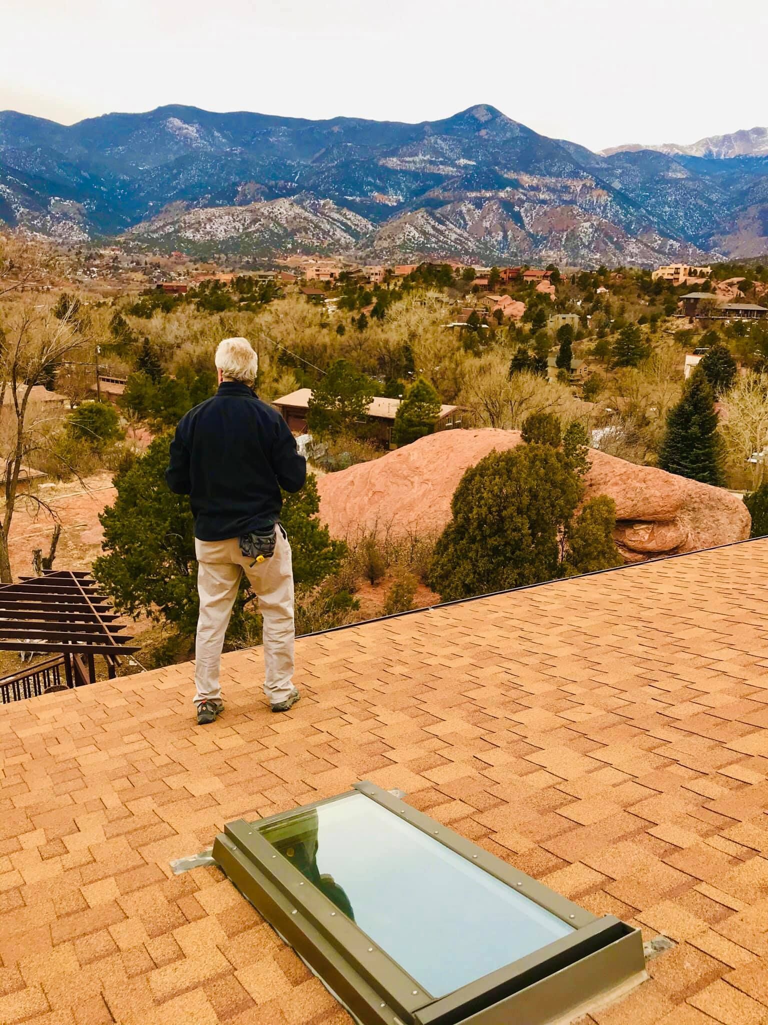 Man on a red-tiled roof looking at a mountain range.  Skylight in foreground.