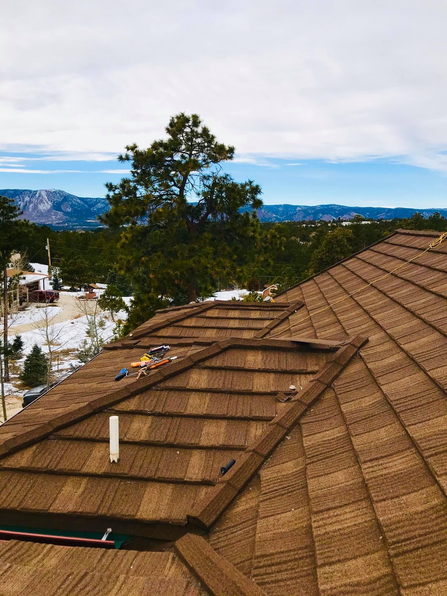 Brown shingle roof with a scenic mountain view, blue sky, and trees.