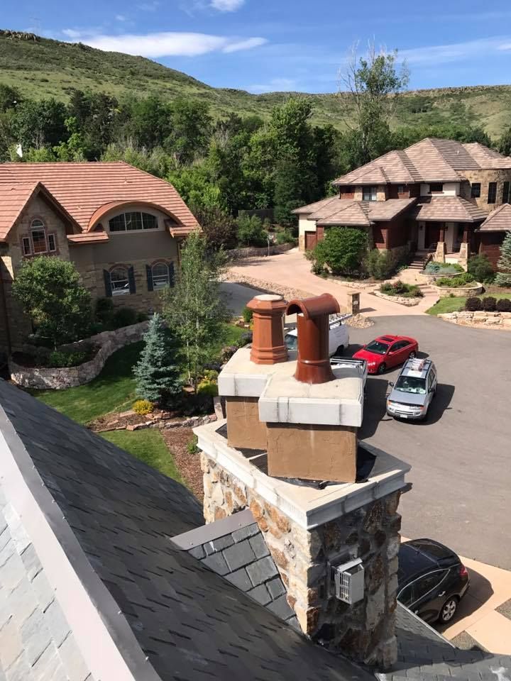 Chimney with terracotta caps; view of houses, cars, and green hills under a blue sky.