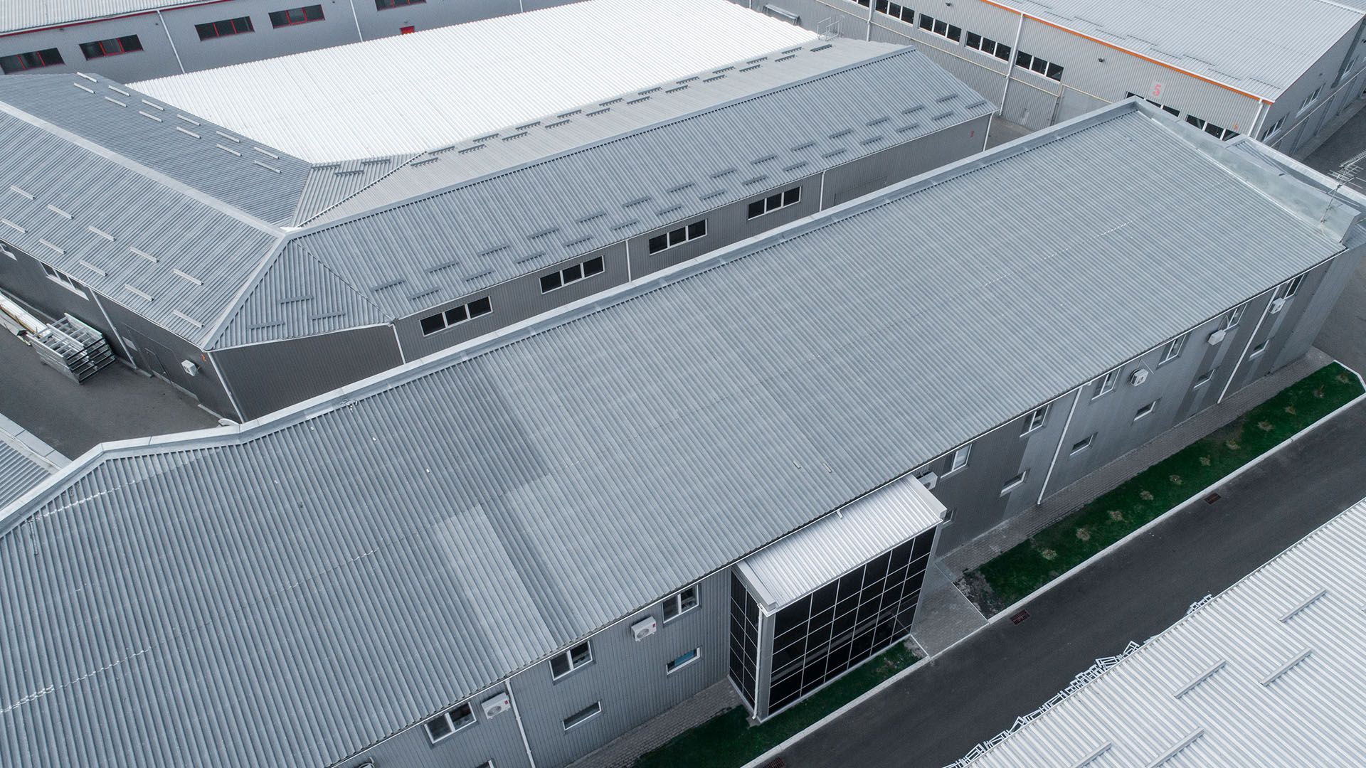 Aerial view of several gray industrial buildings with sloped metal roofs.