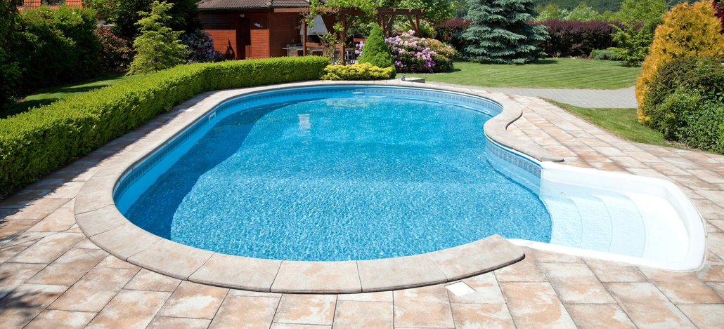Backyard pool with bright blue water, stone patio, and lush green landscaping.