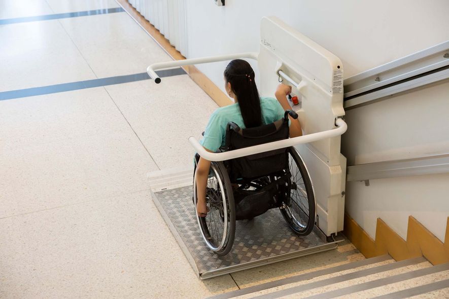 Person in a wheelchair descending a stair lift beside a staircase indoors