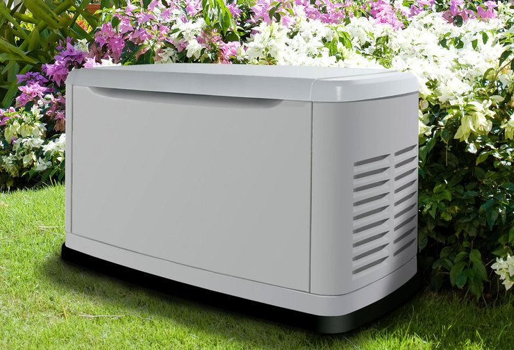 White outdoor generator beside flowering bushes on a grassy lawn