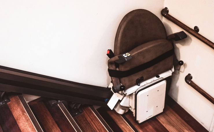 Stairlift chair with beige seat and white footrest beside a wooden staircase.