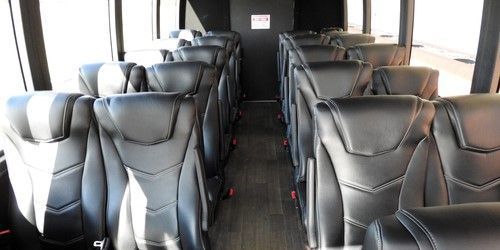 The inside of a bus with rows of black leather seats.