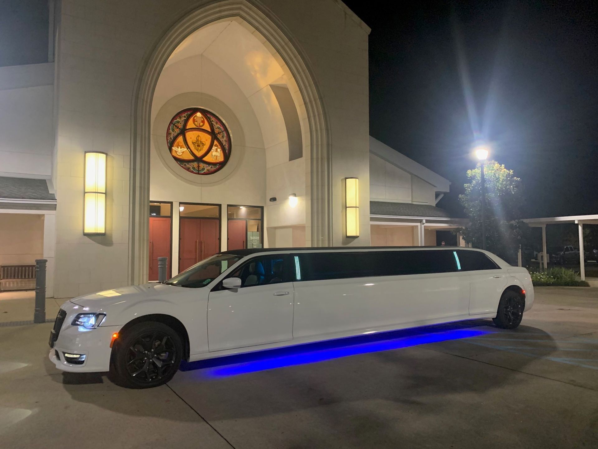 A white limousine is parked in front of a church at night.