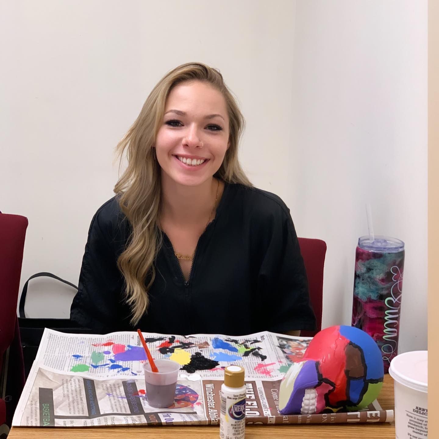 A woman sits at a table with a bottle of acrylic paint