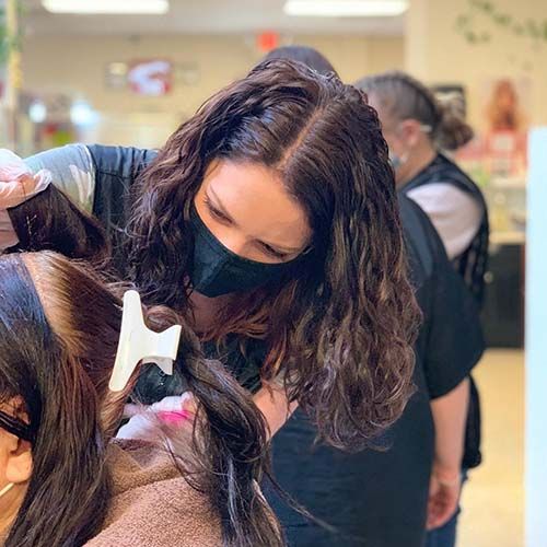 A woman wearing a mask is cutting a woman 's hair in a salon.