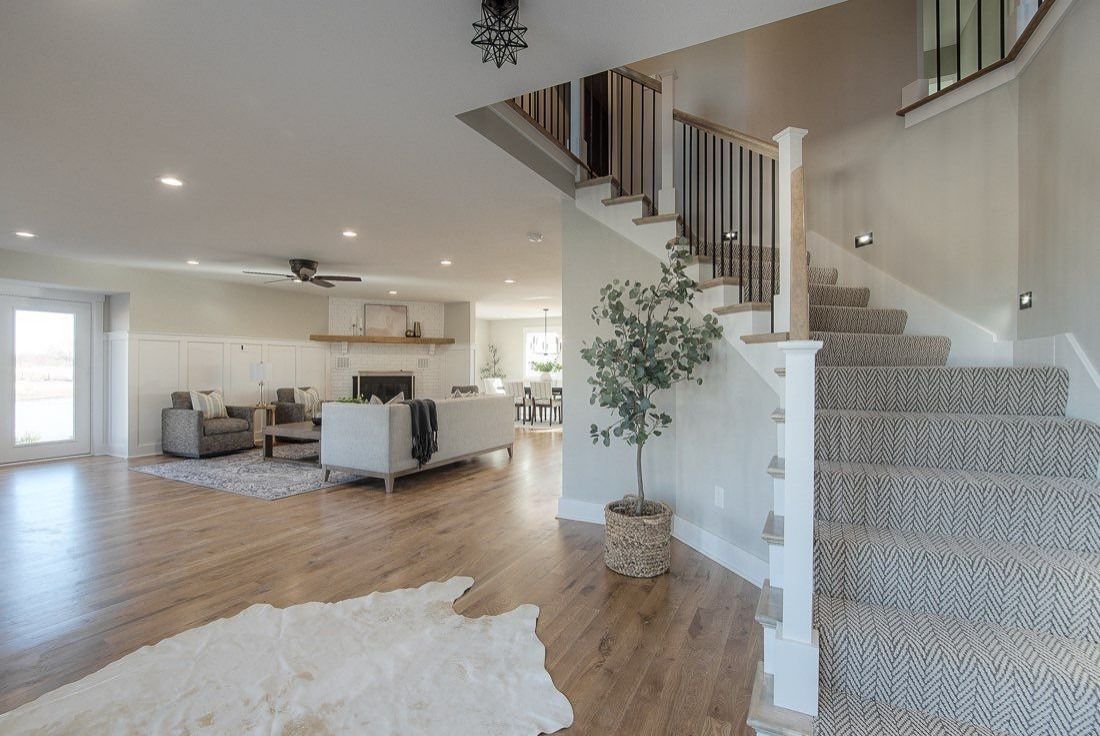 Bright open living room with white sofas, wood floors, and a carpeted staircase leading upstairs