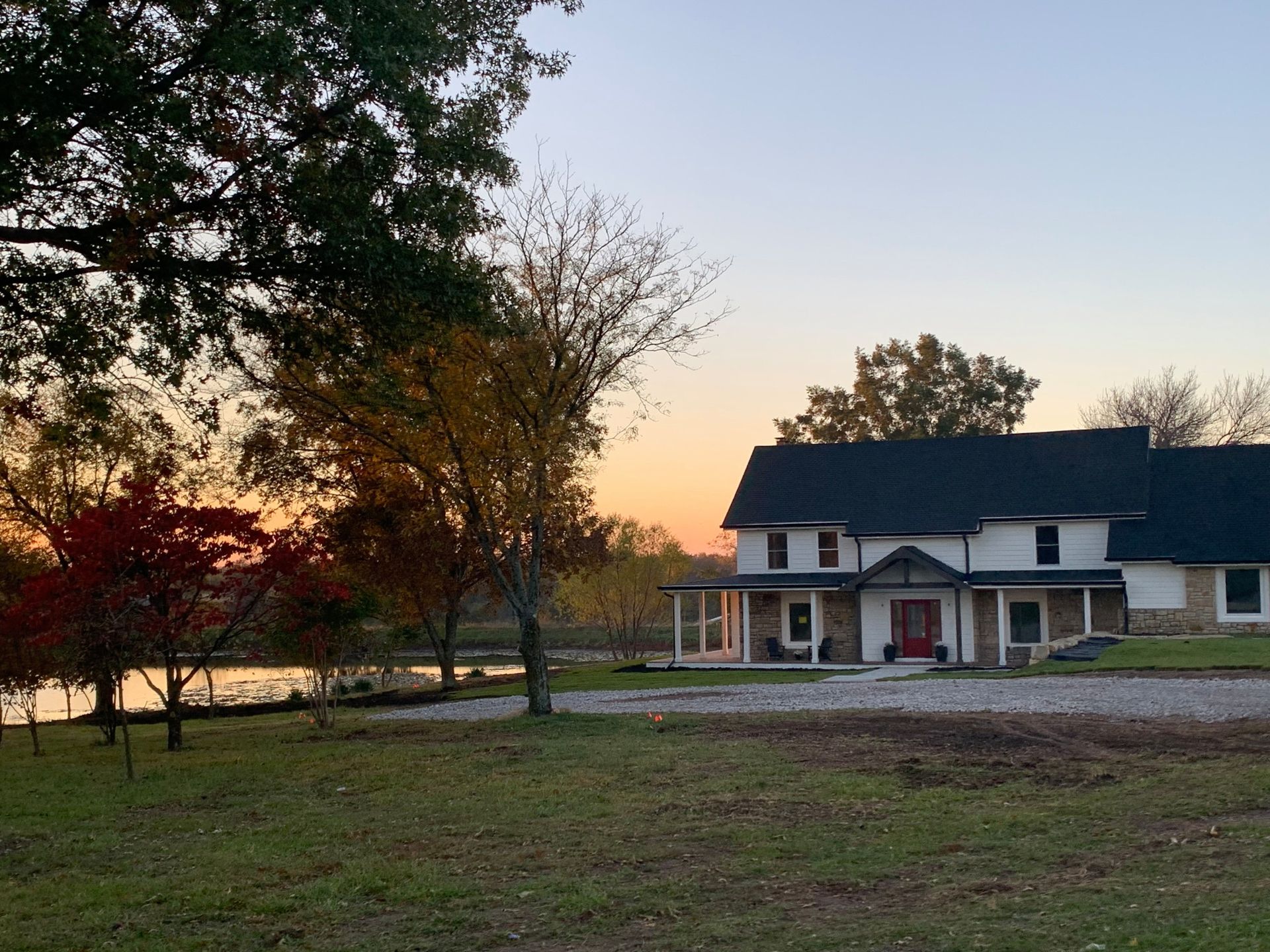Rural house at sunset with a red door, trees, and a grassy yard