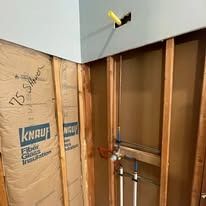 Partially renovated wall with exposed framing, insulation, and plumbing inside a bathroom nook