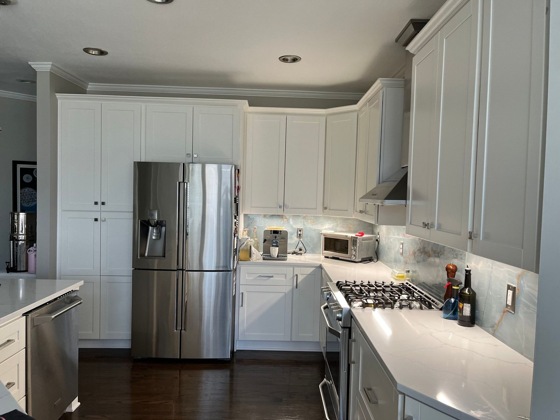 Bright white modern kitchen with stainless steel refrigerator, island, and gas stove beneath cabinets.