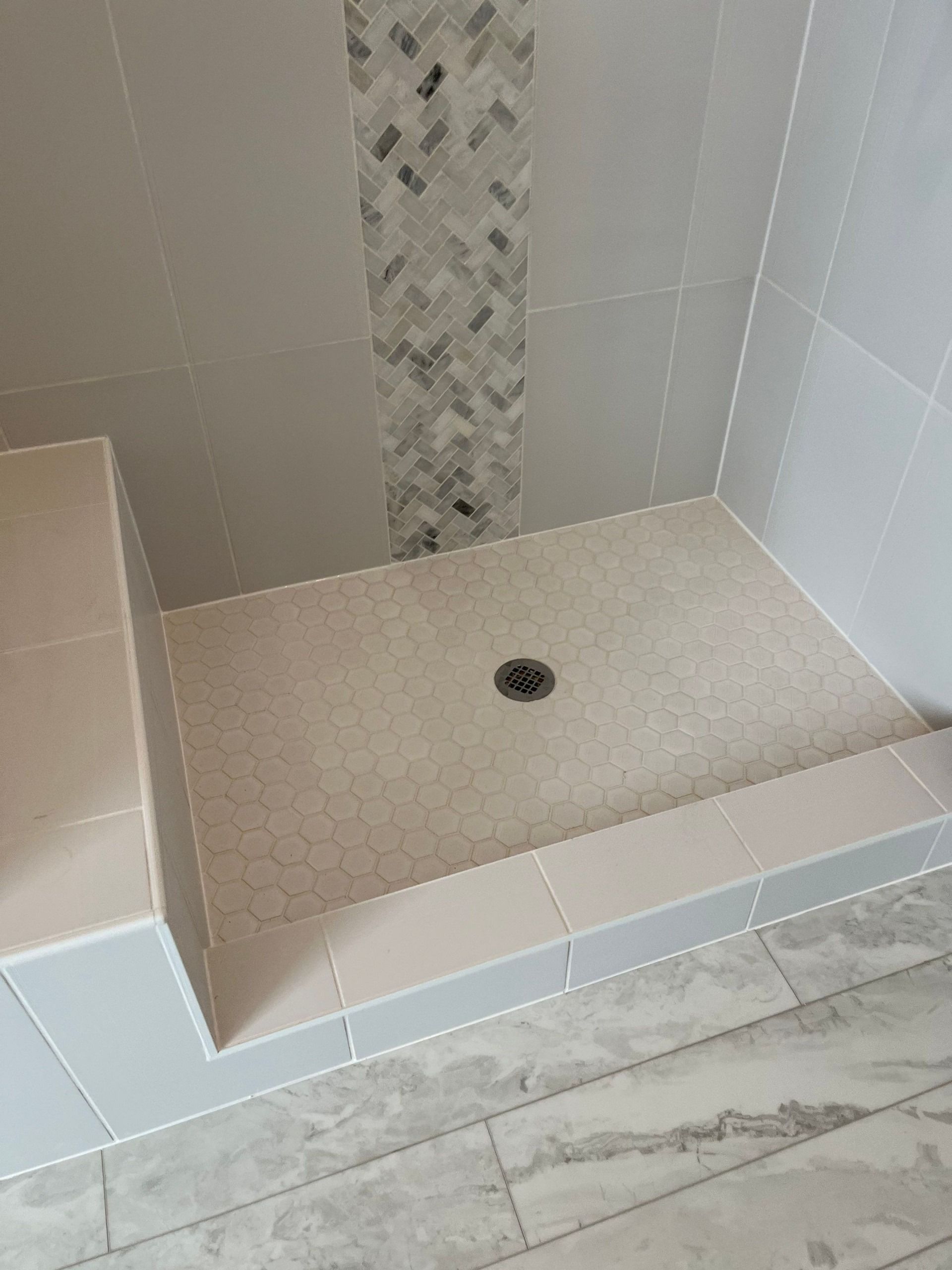 Empty tiled shower stall with a built-in bench and central drain.
