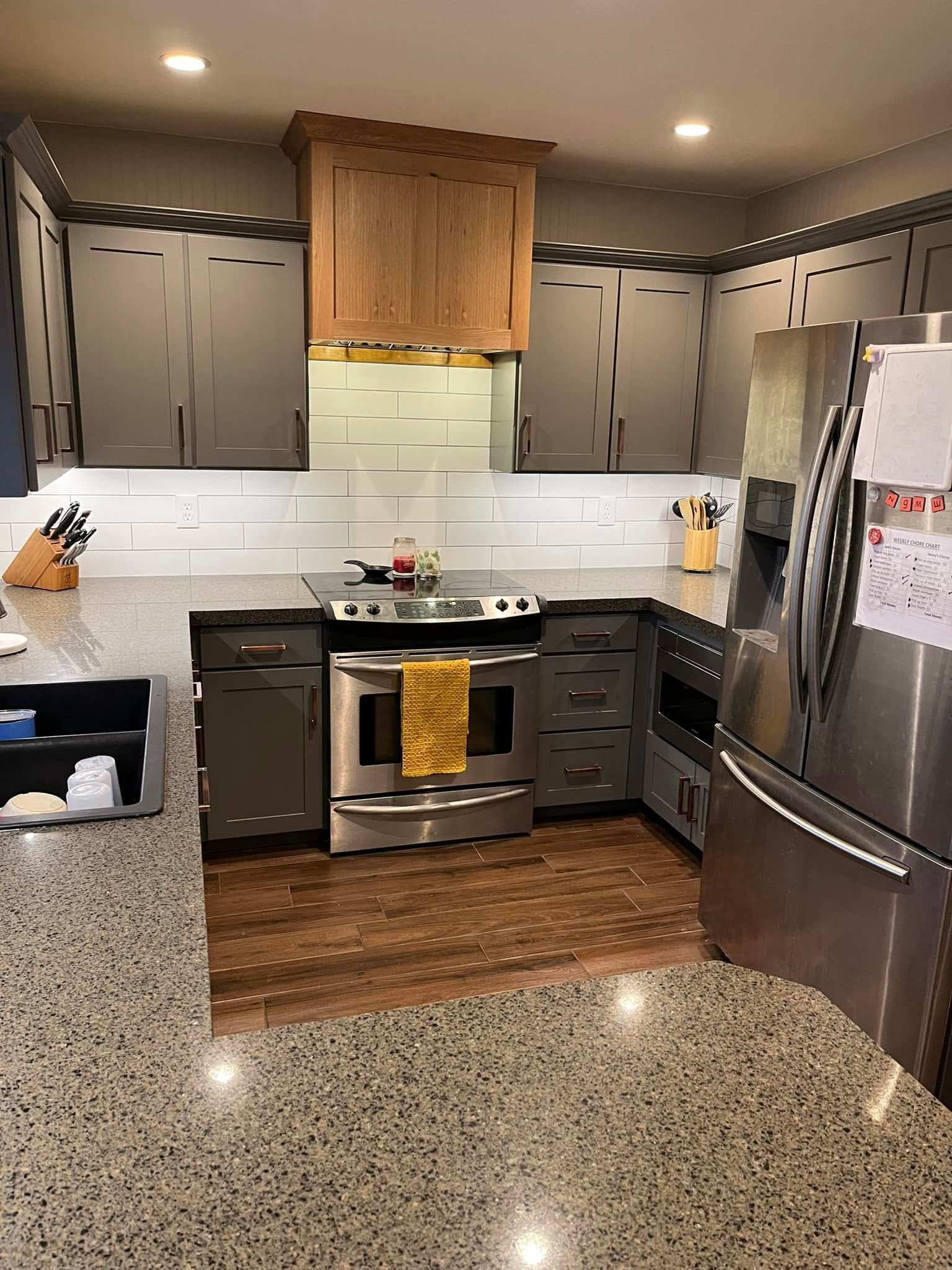 Modern kitchen with gray cabinets, stainless steel appliances, white backsplash, and speckled granite island.