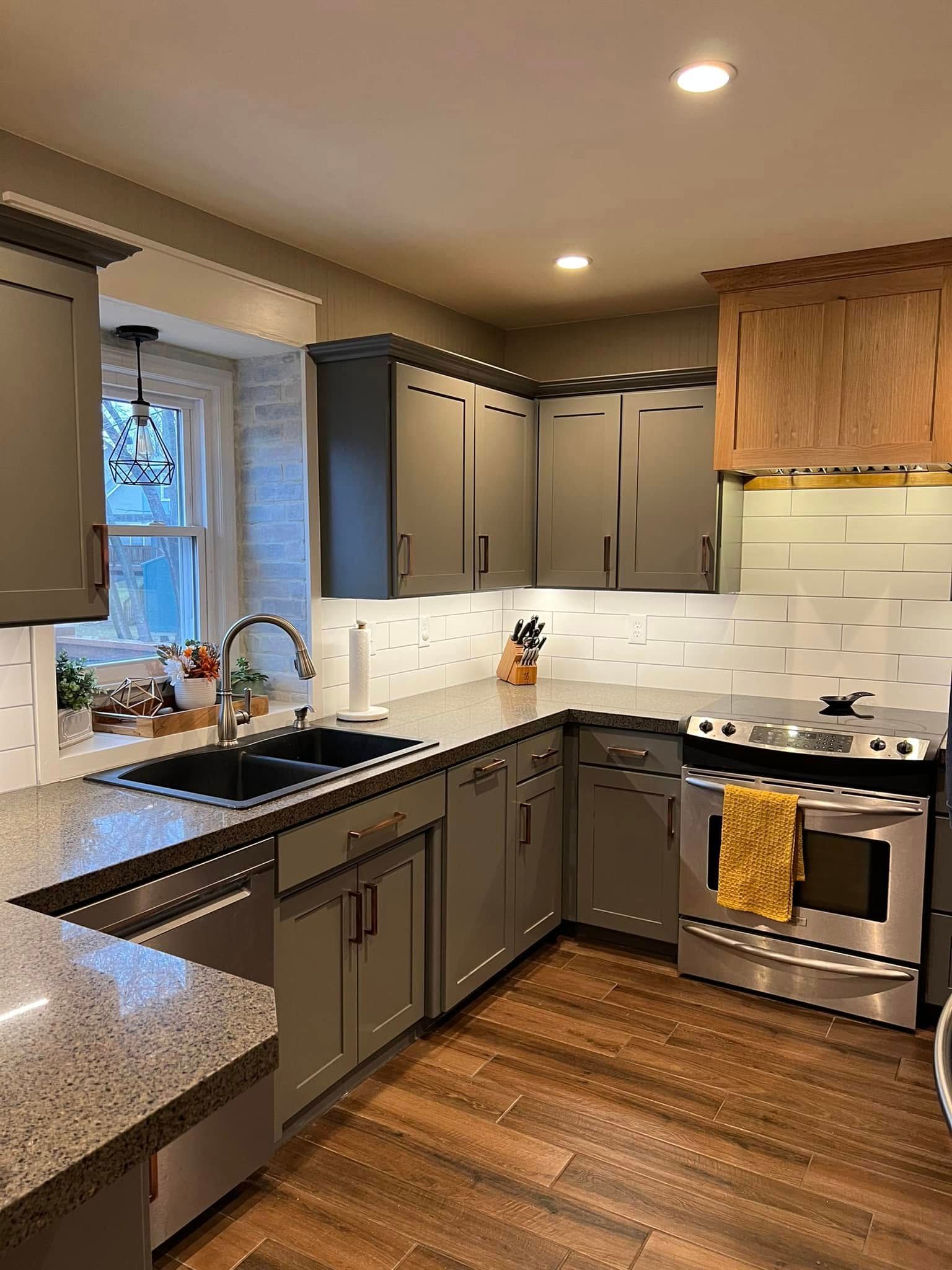 Modern kitchen with gray cabinets, white tile backsplash, wood floor, and stainless steel appliances