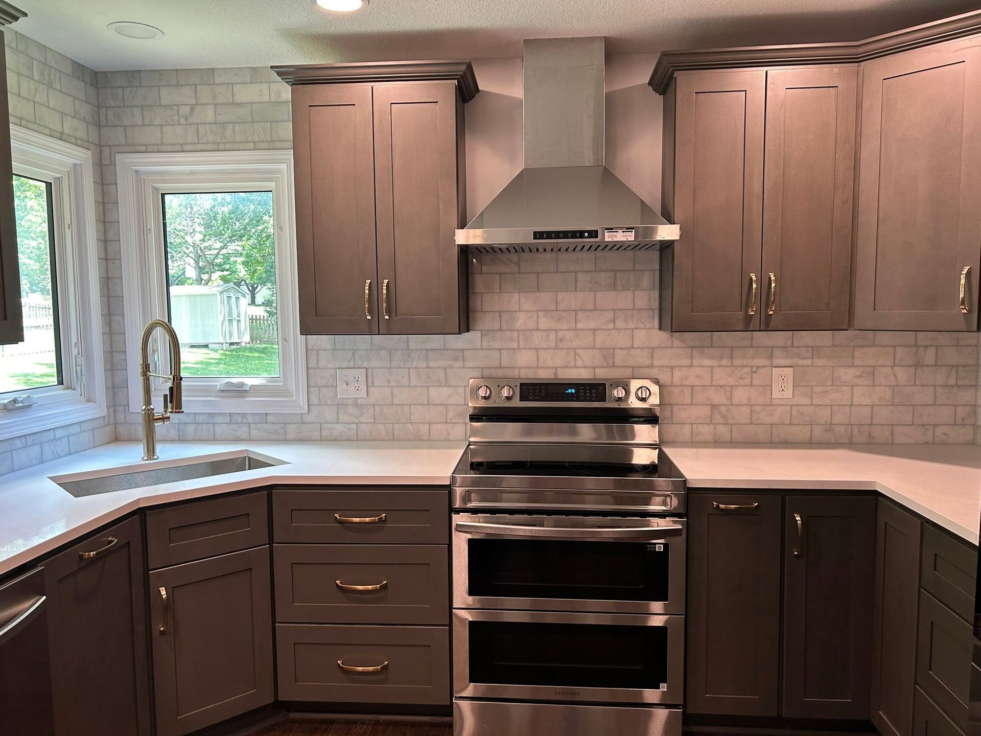 Modern kitchen with dark wood cabinets, white countertops, stainless steel range, and tiled backsplash