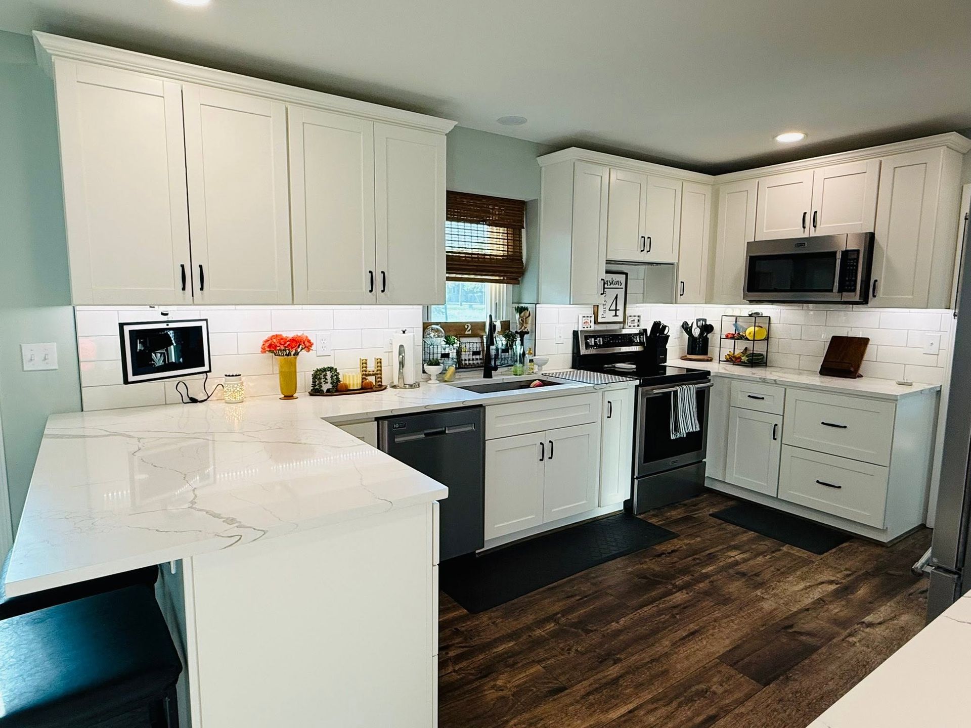 Bright modern kitchen with white cabinets, dark wood floor, and stainless steel appliances.
