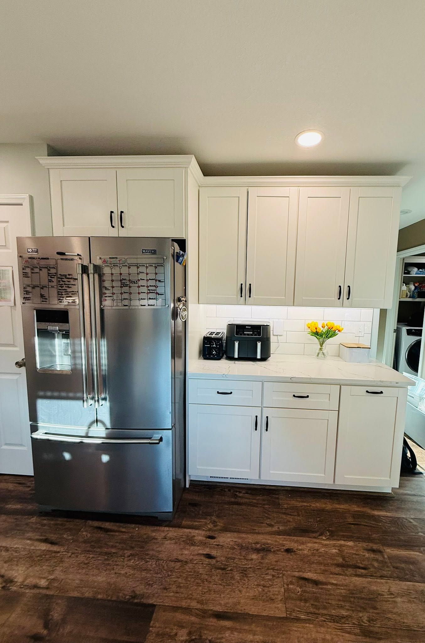 Bright white kitchen with stainless steel refrigerator, cabinets, countertops, and dark wood floor