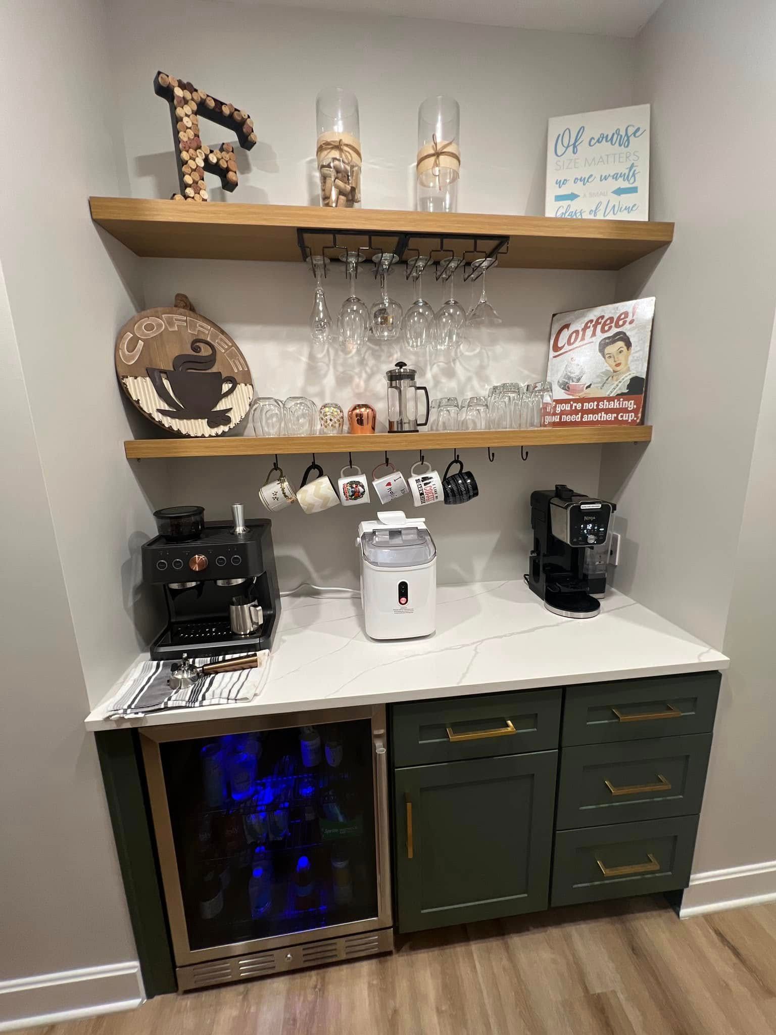 Coffee station with shelves, mugs, a coffee maker, and a mini fridge on dark cabinets against a gray wall