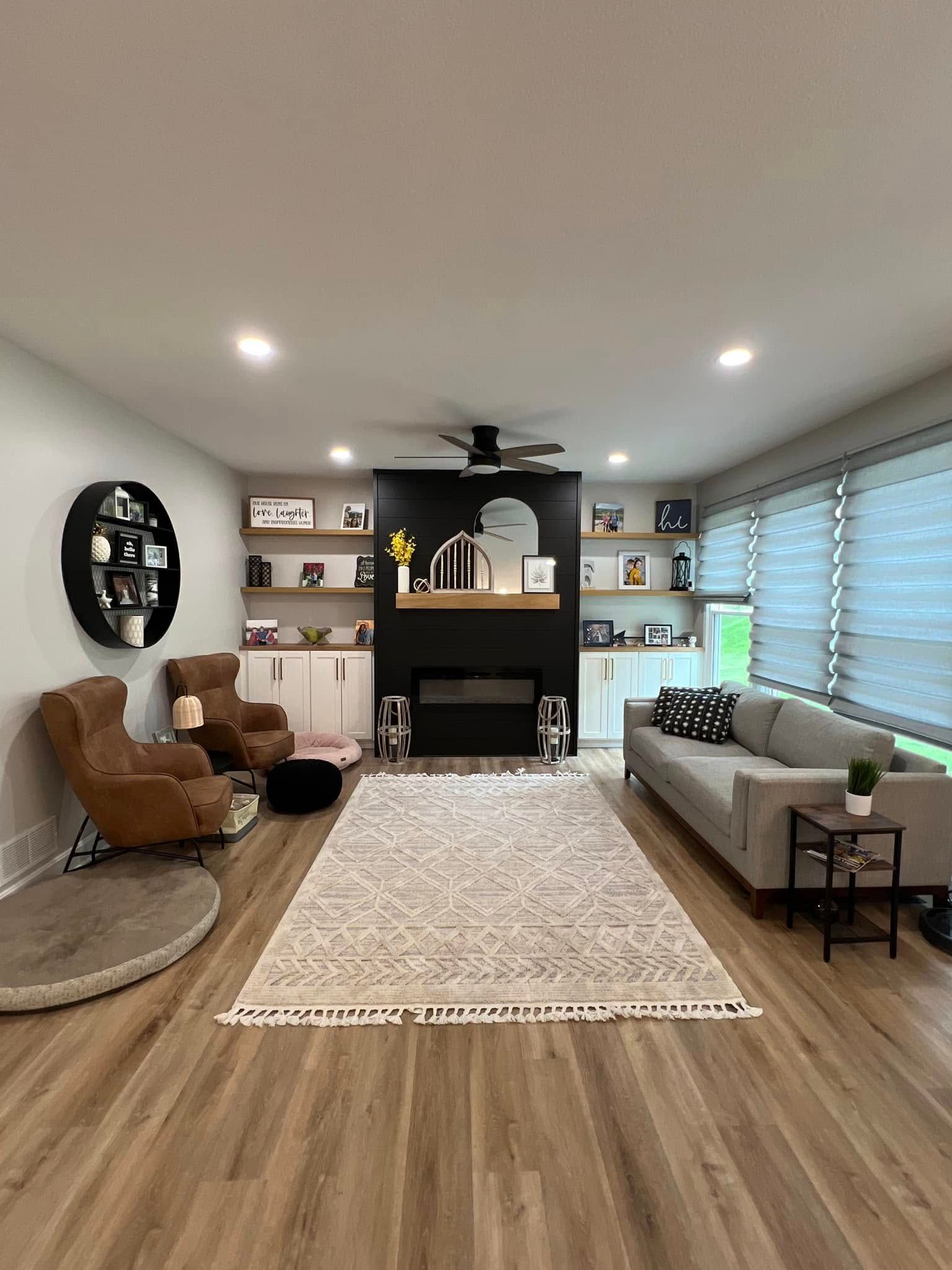 Modern living room with fireplace, white sofa, tan chair, bookshelves, rug, and wood flooring