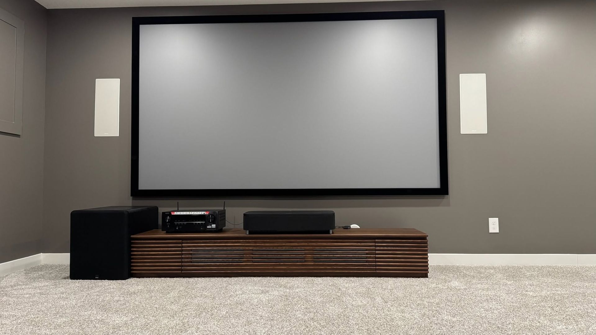 Minimal home theater with a large blank projector screen, wall speakers, and low media console.