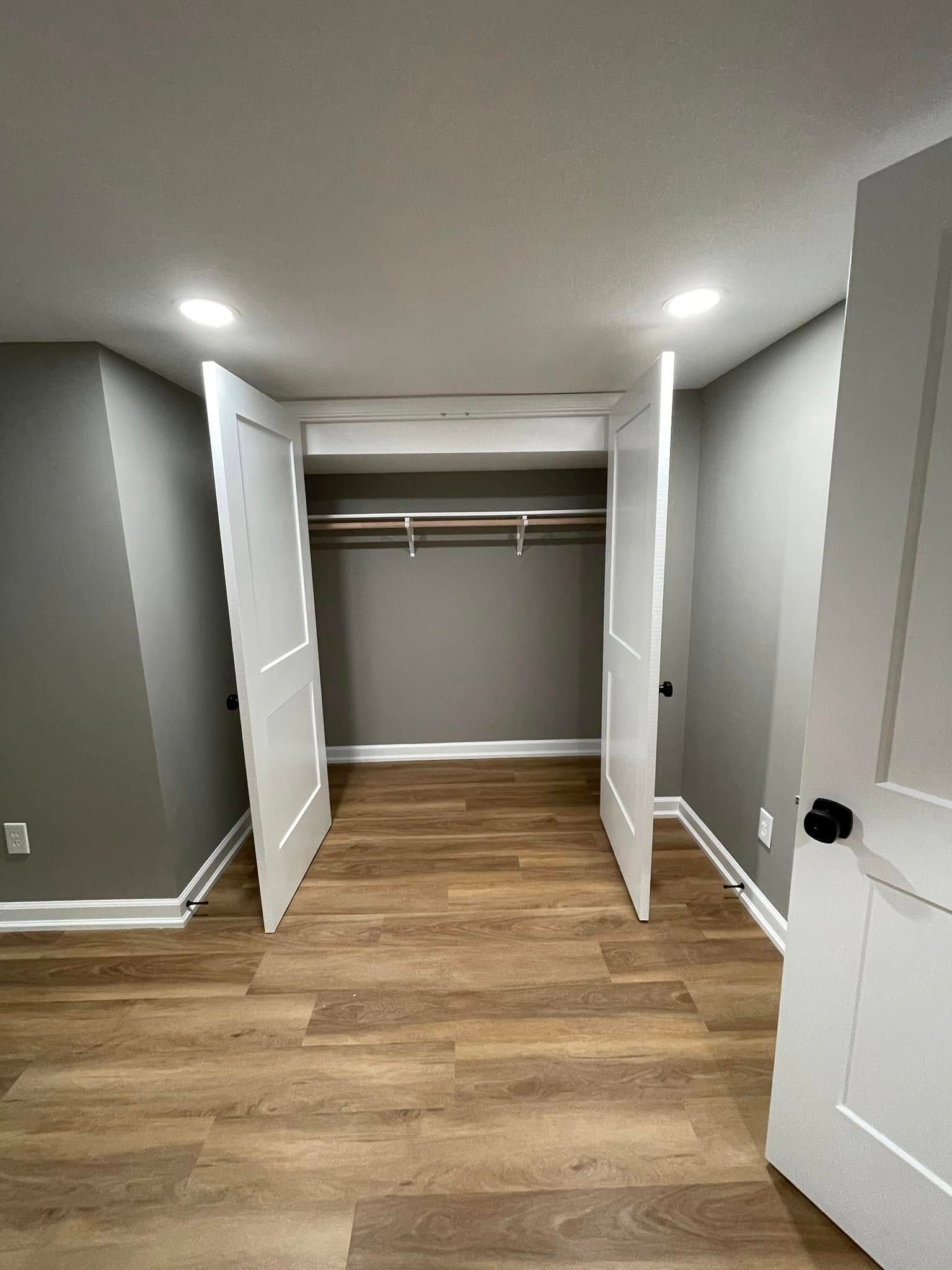 Open closet with white double doors, wooden floor, and gray walls in a small empty room